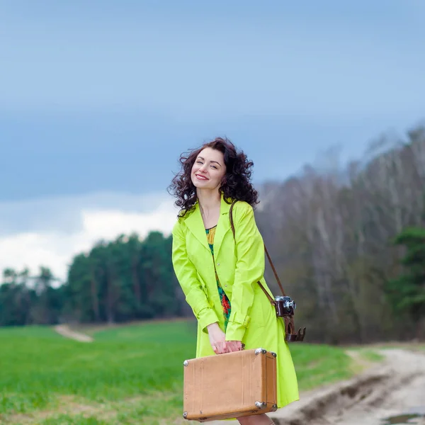 Hipster girl with a suitcase and a retro camera on the road — Stock Photo, Image