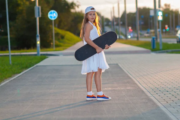 Teenage girl riding skateboard on the evening street — Stock Photo, Image