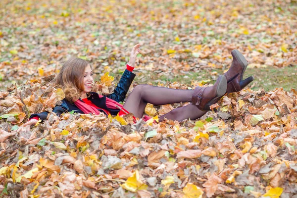 Alegre positivo soñadora chica acostada entre las hojas en el parque — Foto de Stock