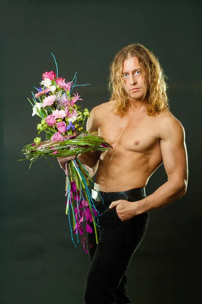 Hombre musculoso varonil con el pelo largo sostiene en las manos un ramo de flores de diseño — Foto de Stock