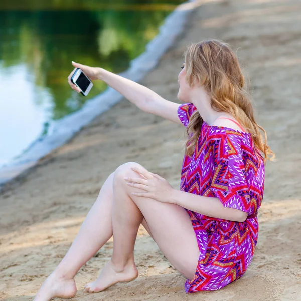 Vacker blond flicka i en bikini på stranden gör selfie. — Stockfoto