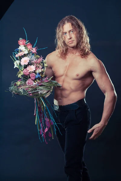 Manly muskularny mężczyzna z długimi włosami trzyma w rękach bukiet kwiatów design — Zdjęcie stockowe