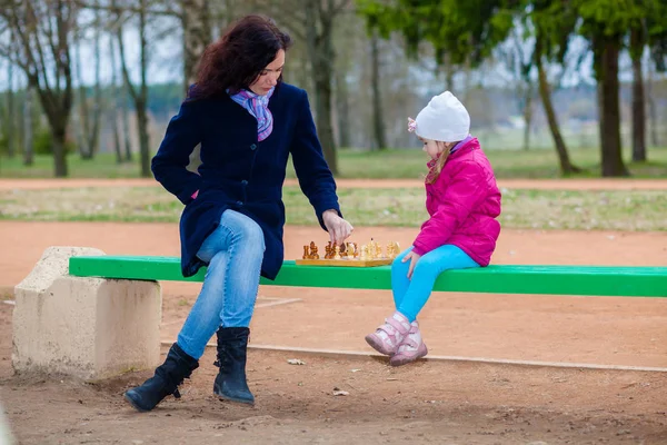 Madre e hija jugando ajedrez en un banco en el parque — Foto de Stock