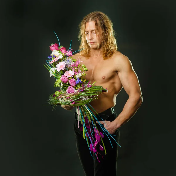 手で花のデザインのブーケを保持している長い髪の男らしい筋肉男 — ストック写真