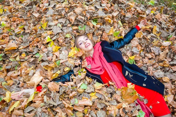 Alegre positivo soñadora chica acostada entre las hojas en el parque — Foto de Stock