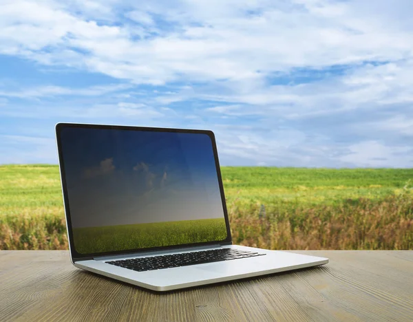 stock image pc on wooden table, fields background