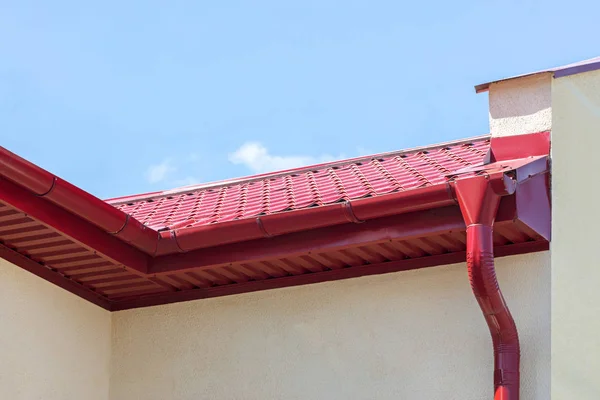 rain gutter with red metal downspout on house roof