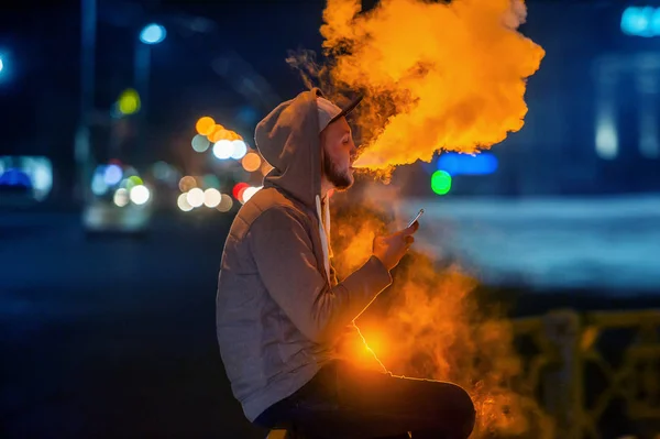 Mladý muž kouření elektronická cigareta při pohledu na telefon — Stock fotografie