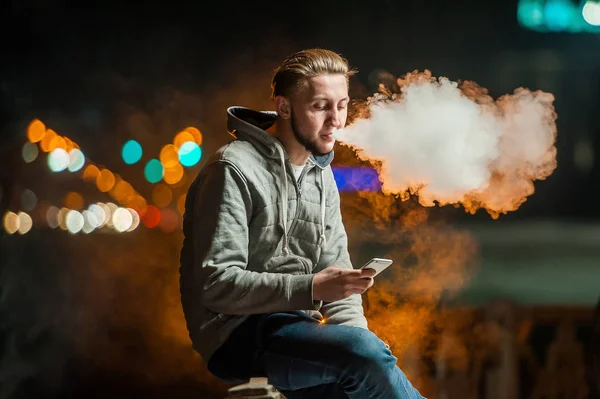 Joven fumando un cigarrillo electrónico mirando el teléfono — Foto de Stock