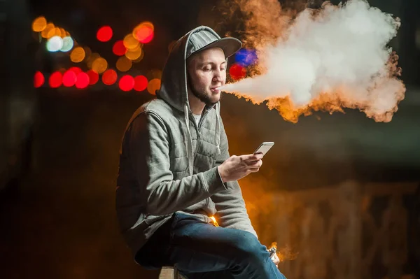 Jongeman roken een elektronische sigaret die kijken naar de telefoon — Stockfoto
