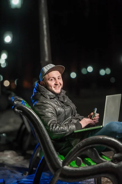 Bel giovanotto con un computer su una panchina del parco — Foto Stock