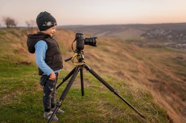 Bir çocuk bir tripod ile a fotoğraf makinesi manzara vuruyor.