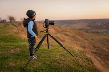Bir çocuk bir tripod ile a fotoğraf makinesi manzara vuruyor.