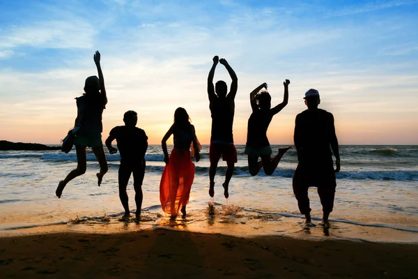 Sechs Menschen springen bei Sonnenuntergang am Strand. Stockbild