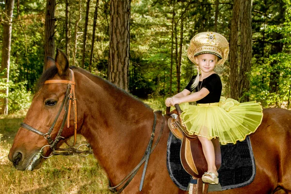 Liten flicka som rider en häst i skogen — Stockfoto