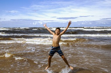Letonya 'nın Jurmala şehrinde aydınlık bir yaz gününde Baltık Denizi' nin dalgalarında zıplayan mutlu çocuk. Yaz tatili kavramı.