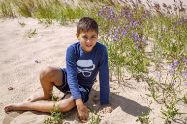 Çocuk Letonya, Jurmala 'da Baltık Denizi kıyısındaki kum tepelerinde kumlu oynuyor.