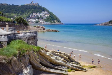İspanya, SAN SEBASTIAN, MAYIS, 10, 2018 - San Sebastian, Donostia, İspanya 'daki Igueldo Dağı' nın arka planında Atlantik Okyanusu 'nun alçak gelgitinden sonra insanlar Playa de La Concha plajının tadını çıkarıyor