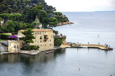 FRANCE, SAIN JEAN CAP FERRAT, AĞUSTOS, 2013 - Sain Jean Cap Ferrat 'ta ormanla kaplı bir dağın arka planında sessiz bir lagündeki özel şato. Fransa