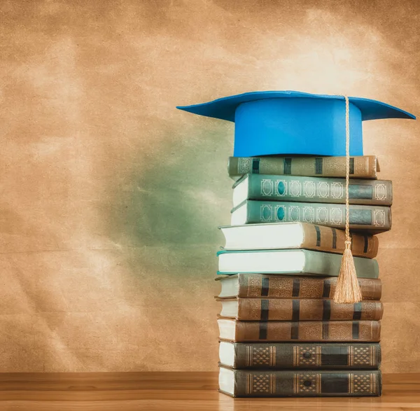 Graduation mortarboard on top of stack of books on abstract back — Stock Photo, Image