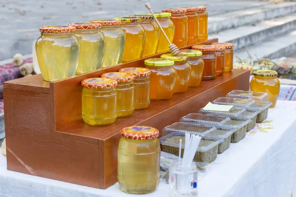 Surtido de tarros de miel en el puesto de mercado. Venta de miel natural en feria al aire libre . — Foto de Stock