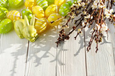 Tatlı Paskalya sembolleri. Renkli sarı, yeşil yumurta ve beyaz arka planda komik tavşan.