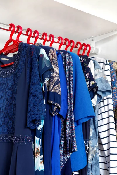 Modern closet with row of cloths hanging in white wardrobe.Choice of fashion clothes of blue colors on red hangers