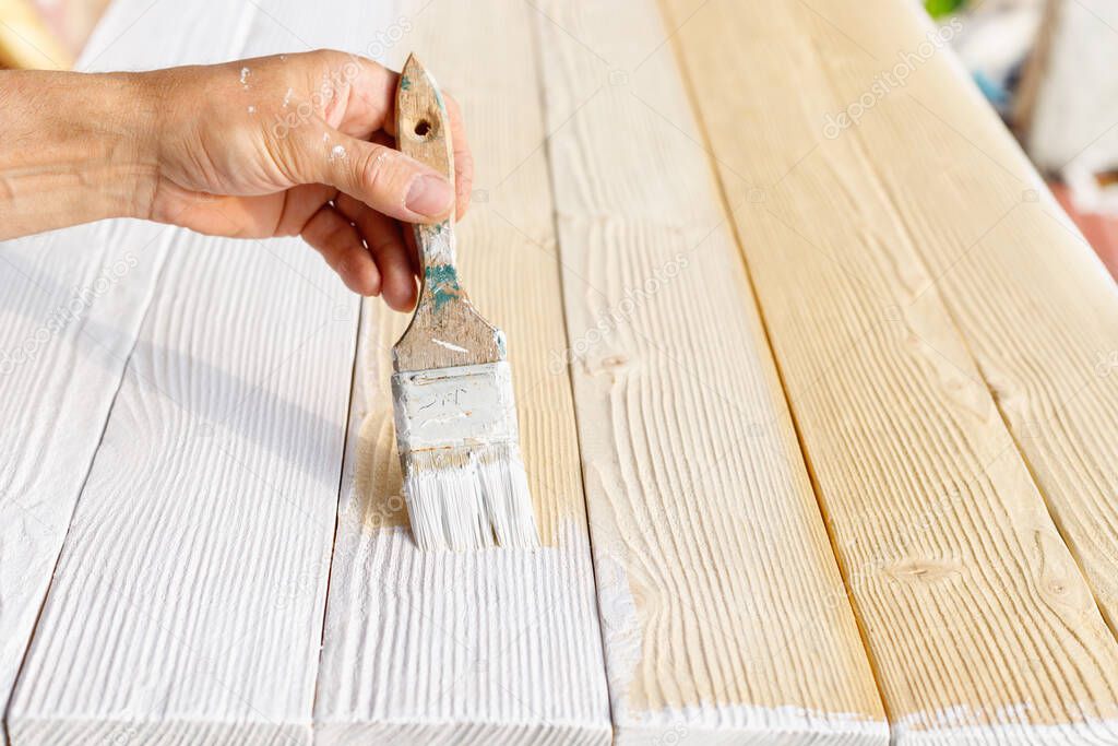 Worker painting white wooden furniture outdoor. Hand with brush closeup