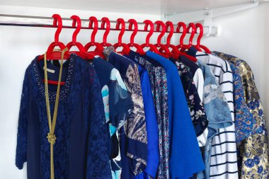 Beyaz gardıropta asılı kıyafetleri olan modern dolap. Kırmızı askılarda mavi renkli moda kıyafetleri.