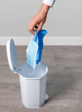 Adam kullanılmış eldivenleri ve maskeyi koronavirüs salgınından sonra kovaya atıyor. Kavram