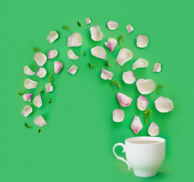 Kavram ya da yaratıcı fikir, çay saati demektir. Narin pembe gül yaprakları ve yeşil kağıt arka planda beyaz porselen bardak.