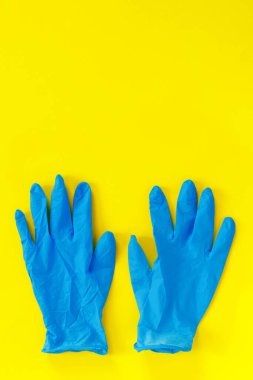 Mavi tıbbi eldiven ve kağıt sarısı arka planda maske. Koronavirüs salgını