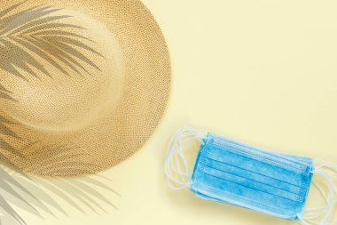 Kağıt bej arka plan, hasır şapka ve mavi tıbbi maskeler. Kavramsal metin: 