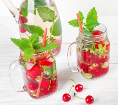 Taze taze meyve suyu, çilek, frenk üzümü ve Bektaşi üzümü beyaz ahşap masada.