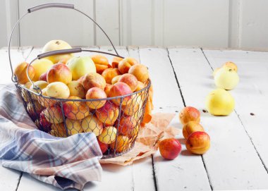 Olgun taze kayısılar ve elmalar dokunmuş metal sepetin içinde odasındaki ahşap masanın üzerinde.