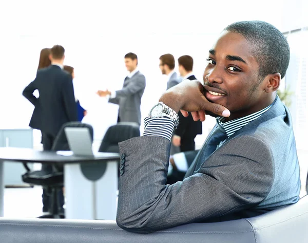 Porträt eines lächelnden afrikanisch-amerikanischen Geschäftsmannes mit Führungskräften im Hintergrund — Stockfoto
