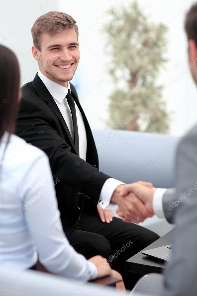 Two happy young men shaking hands while sitting at the office