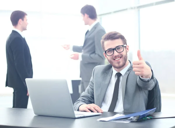 Bel giovane uomo d'affari con persone in background alla riunione d'ufficio. mostrando pollici in su — Foto Stock