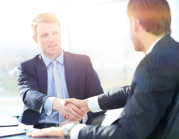 Collega's zitten aan een tafel tijdens een ontmoeting met twee mannelijke executives handen schudden — Stockfoto