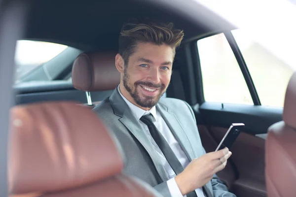 Felice giovane uomo d'affari utilizzando il telefono cellulare nel sedile posteriore della macchina — Foto Stock