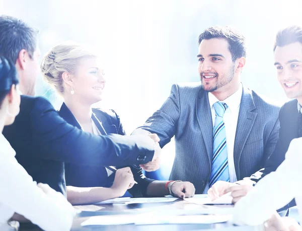 Geschäftskollegen sitzen an einem Tisch während eines Meetings mit zwei männlichen Führungskräften beim Händeschütteln — Stockfoto