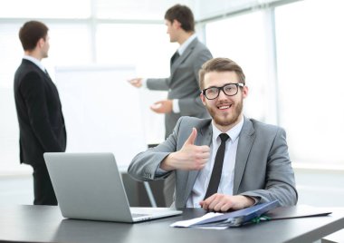 Yönetmen açık bir dizüstü bilgisayar ve kağıtları ile masada oturuyor.