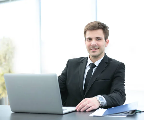 Erfolgreicher Geschäftsmann sitzt hinter einem Schreibtisch mit offenem Laptop — Stockfoto