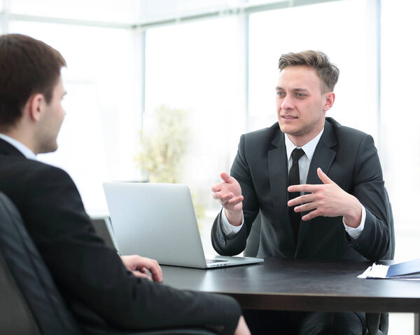 Сотрудник банка сидит за столом и разговаривает с клиентом
