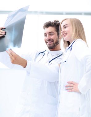 İki doktor röntgen görüntülerini inceliyor, parlak ofiste danışmanlık yapıyorlar.