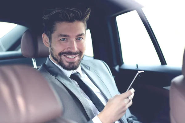 Heureux jeune homme d'affaires en utilisant le téléphone portable dans le siège arrière de la voiture — Photo