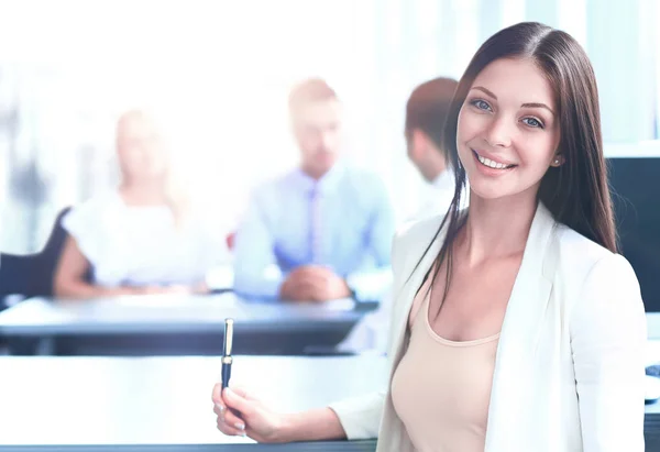 Sonriente mujer de negocios confiada mirando a la cámara con sus colegas en segundo plano en la oficina — Foto de Stock