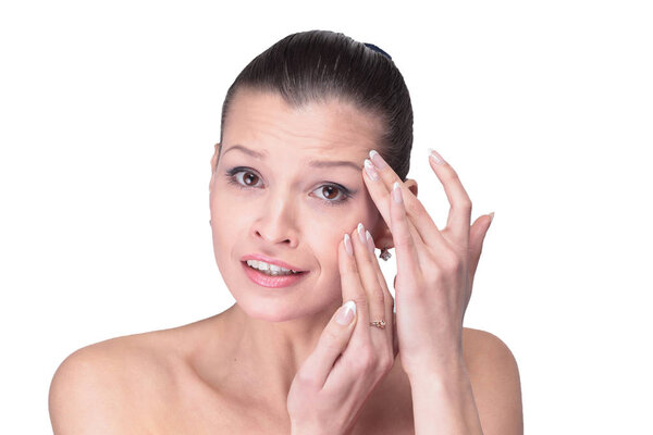 Молодая девушка рассматривает свое лицо и морщины, которые могут появиться изола
