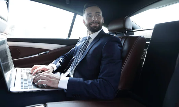 Podnikatel s notebookem sedí na zadním sedadle auta — Stock fotografie