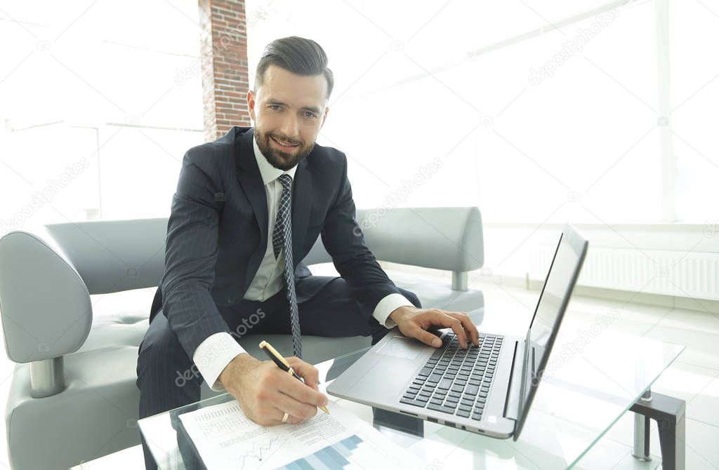 Stylish man working on laptop and making notes in notebook